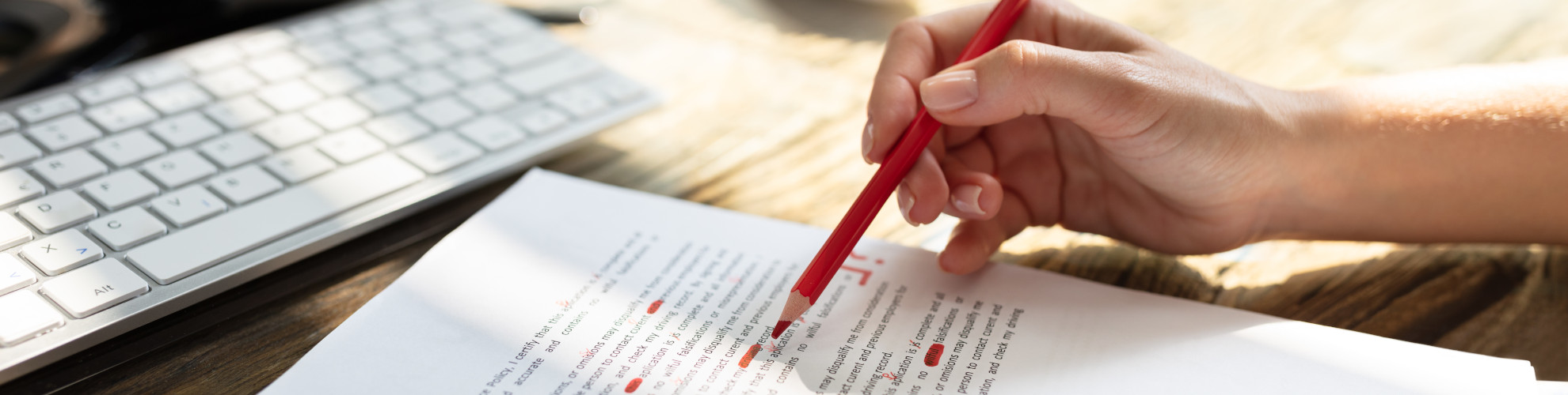 Tastatur und Blatt, daneben die rechte Hand einer Frau mit Rotstift.